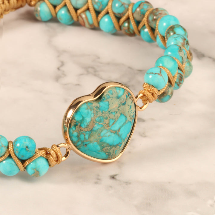 Close-up of a handmade adjustable bracelet featuring turquoise stone beads and a heart-shaped turquoise centerpiece, wrapped in gold-tone accents.