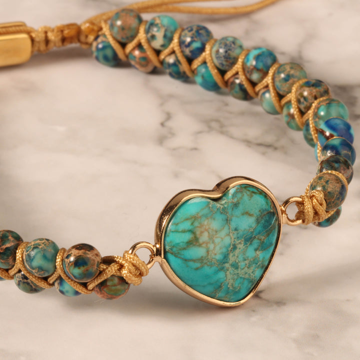 Close-up of a handmade adjustable bracelet featuring turquoise stone beads and a heart-shaped turquoise centerpiece, wrapped in gold-tone accents.