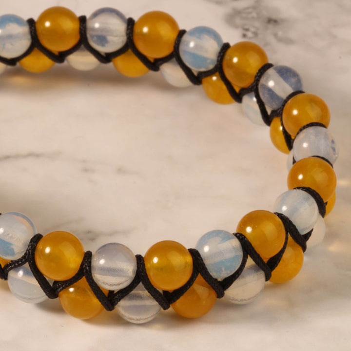 Close-up of a handmade bracelet featuring yellow jade and opalite beads, wrapped with a black cord for a bold and stylish design.