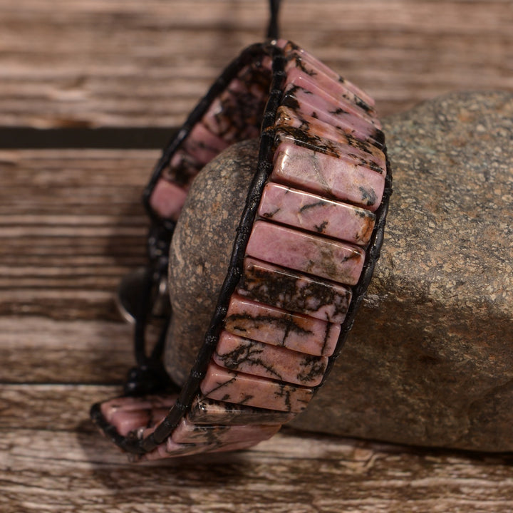 Side view of a handmade adjustable bracelet featuring natural Rhodonite tube stones in pink and black hues, wrapped in black leather cord.